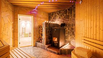A sauna room with a stone wall, wooden benches, and a wood-burning stove.