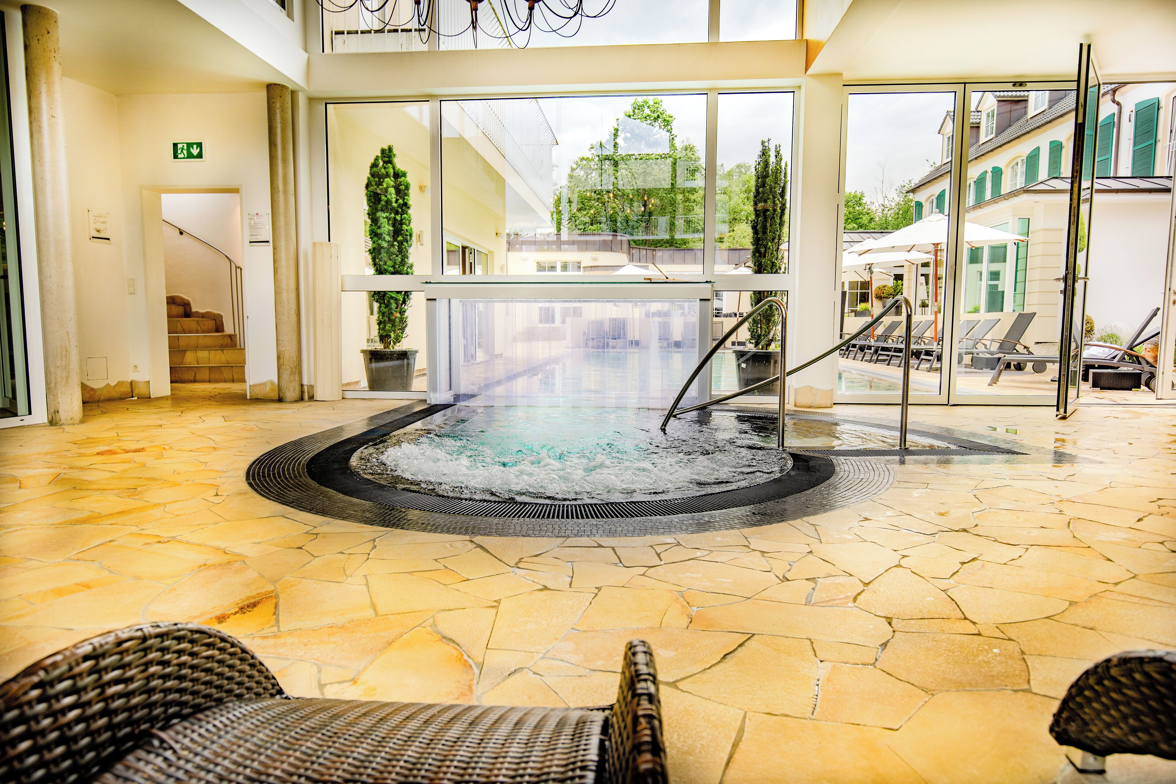 A spa area with a hot tub, stone flooring, wicker chairs, and a view of the outside.