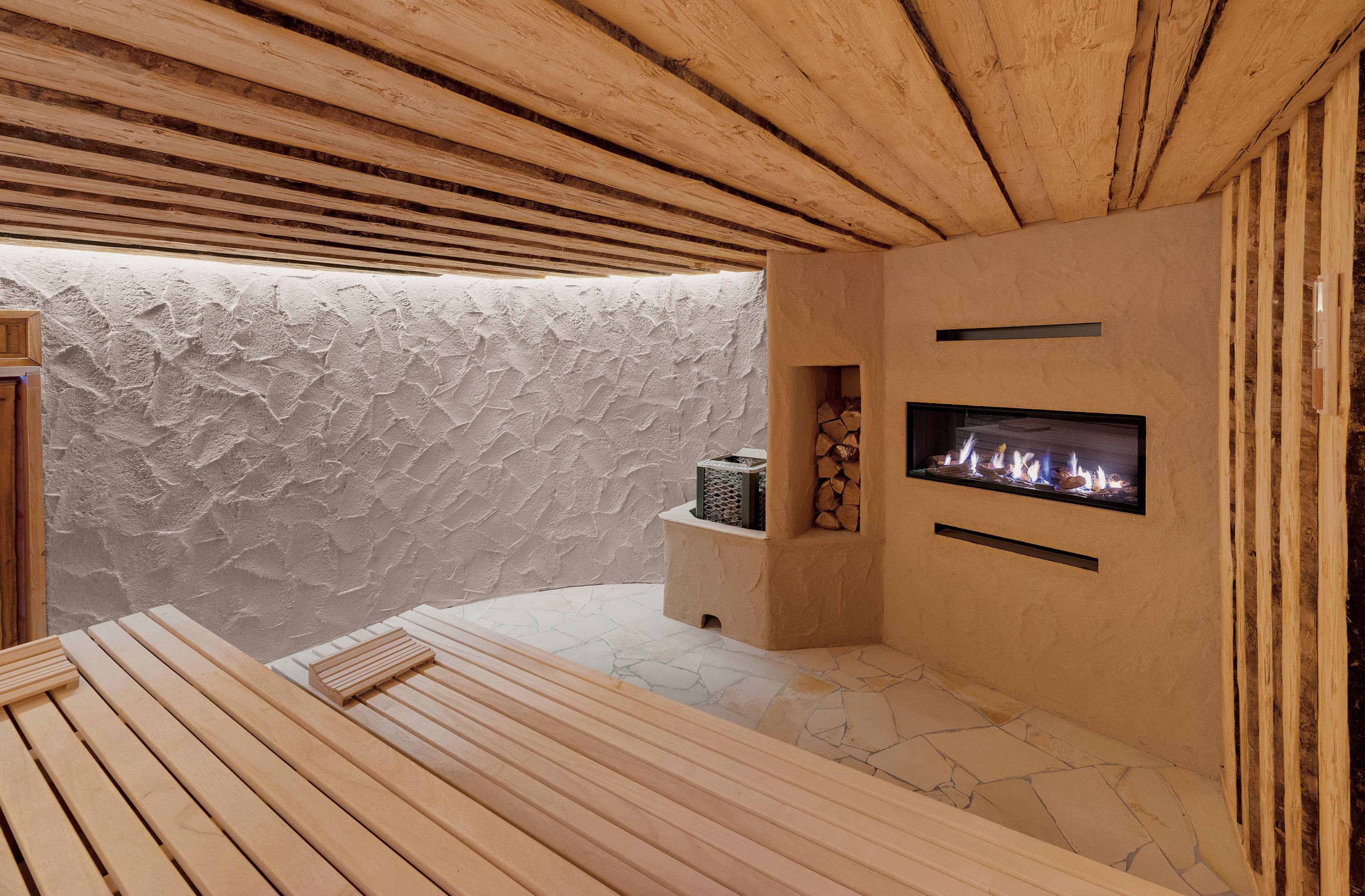 A wooden ceiling, a stone wall, a fireplace, and a wooden bench.