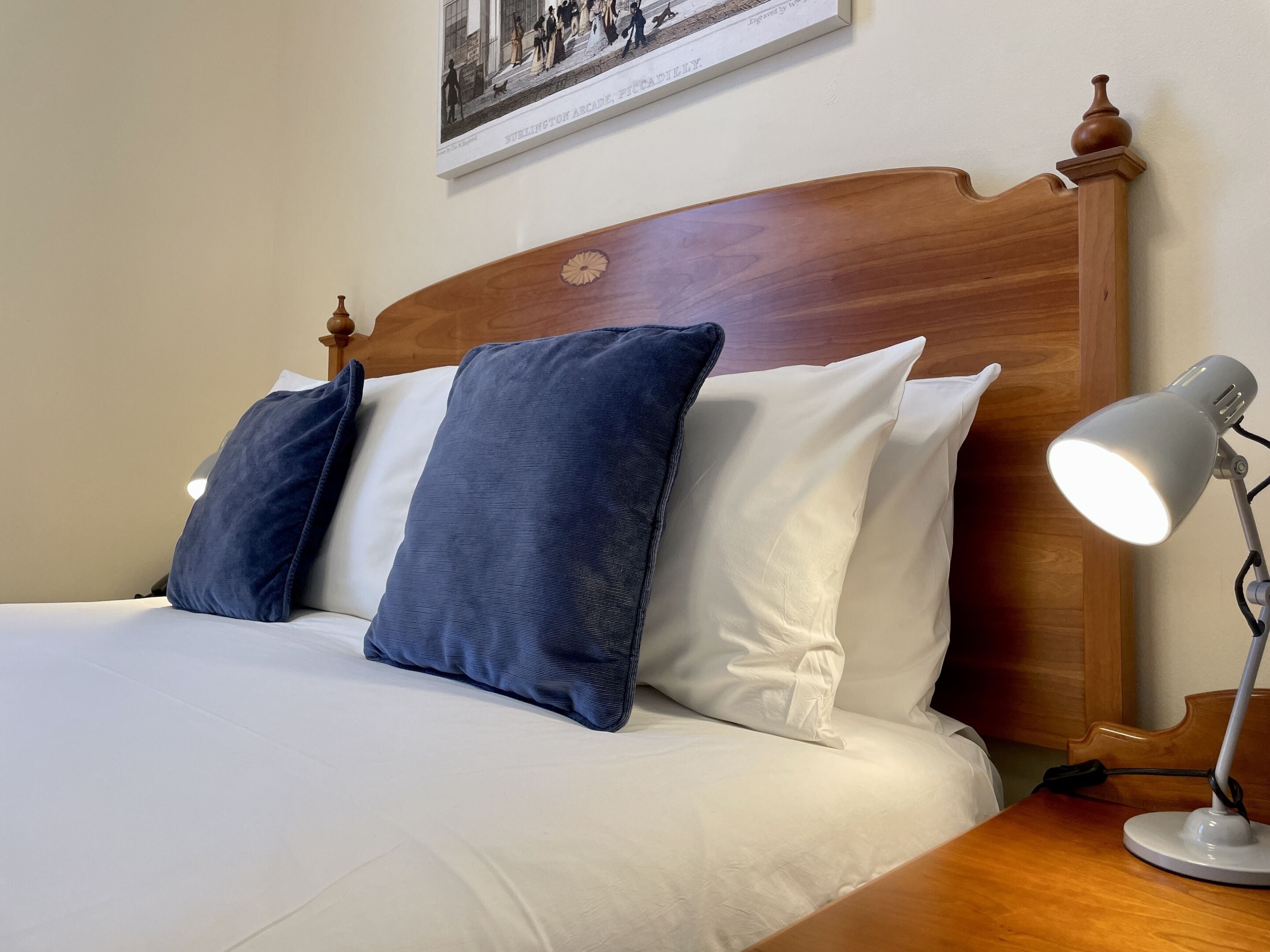 Cama bem arrumada com almofadas azuis e brancas, cabeceira de madeira e mesa de cabeceira com abajur.