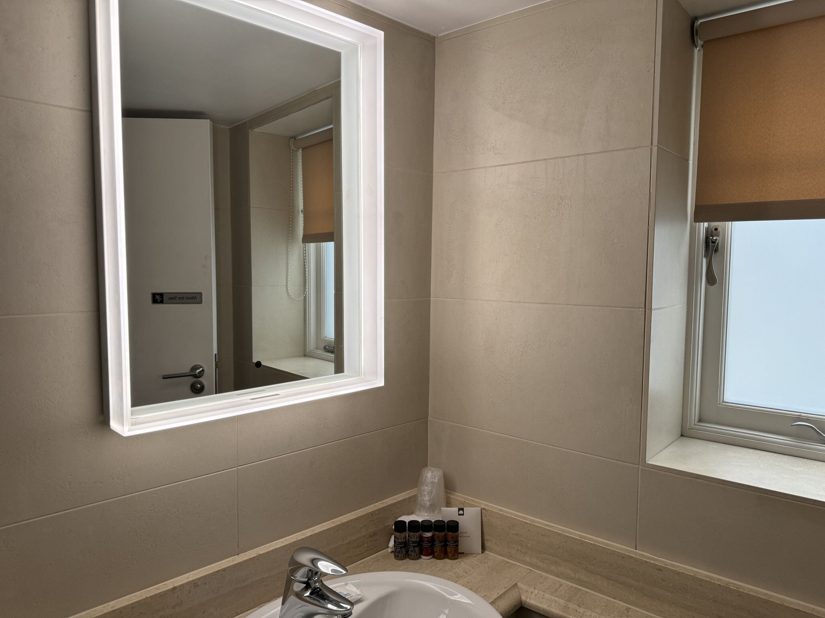 A bathroom with a large mirror, a sink, and a window.