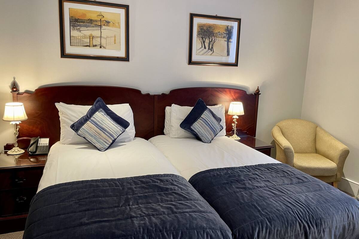 A hotel room with a double bed, two nightstands, a chair, and two framed pictures on the wall.