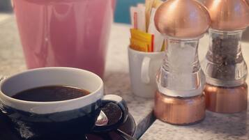 Un plan de travail de cuisine avec une tasse à café, une plante en pot rose, des salières et des poivrières, et un moulin à café.