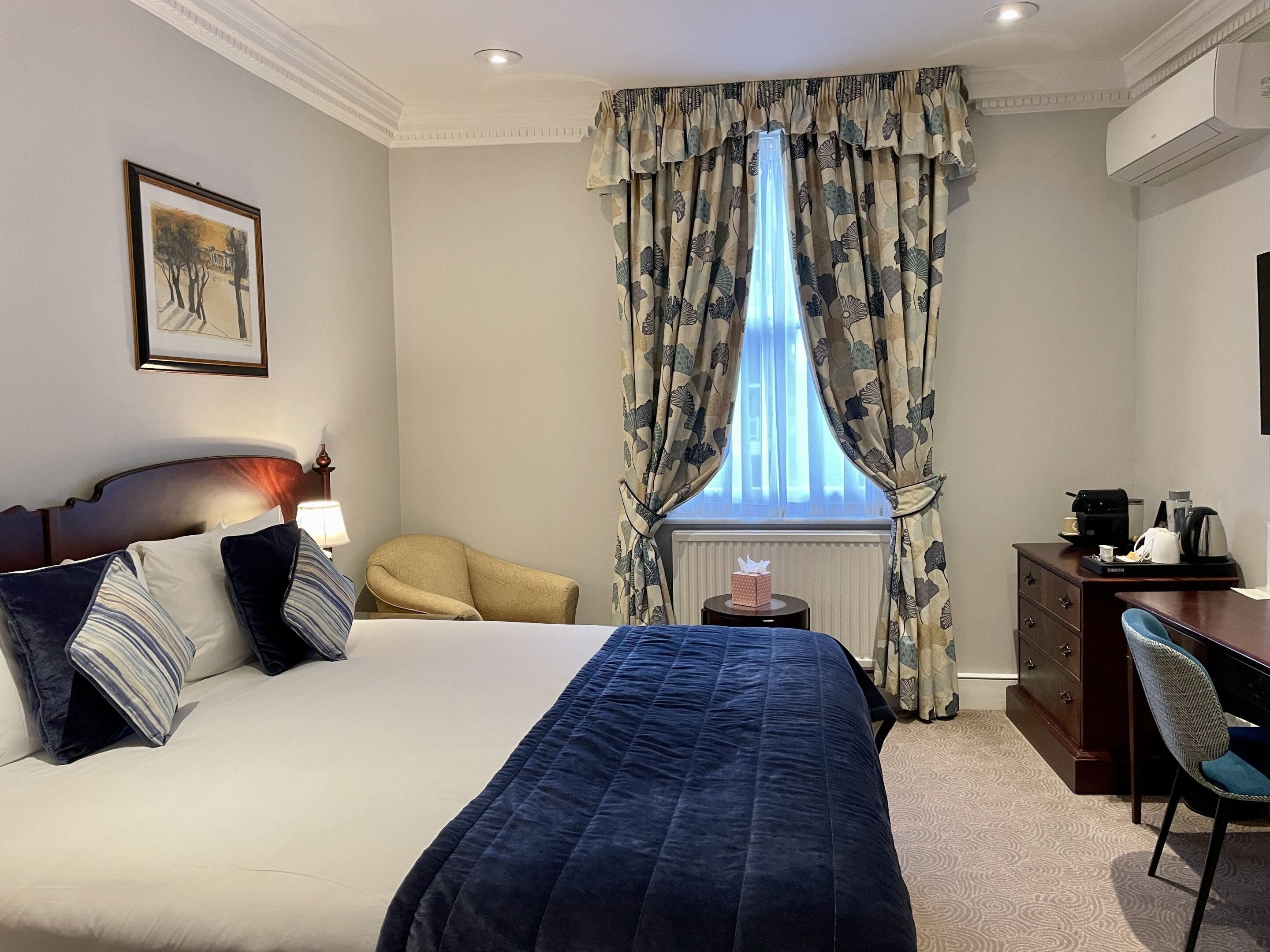 A hotel room with a bed, a chair, a desk, and a window with curtains.