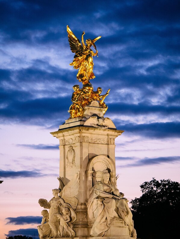 Une statue classique représentant plusieurs personnages, dont un ange, placée au sommet d’une structure ornée de colonnes.