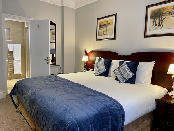 A hotel room with a large bed, a wooden headboard, a bedside table with a lamp, and a framed picture on the wall.