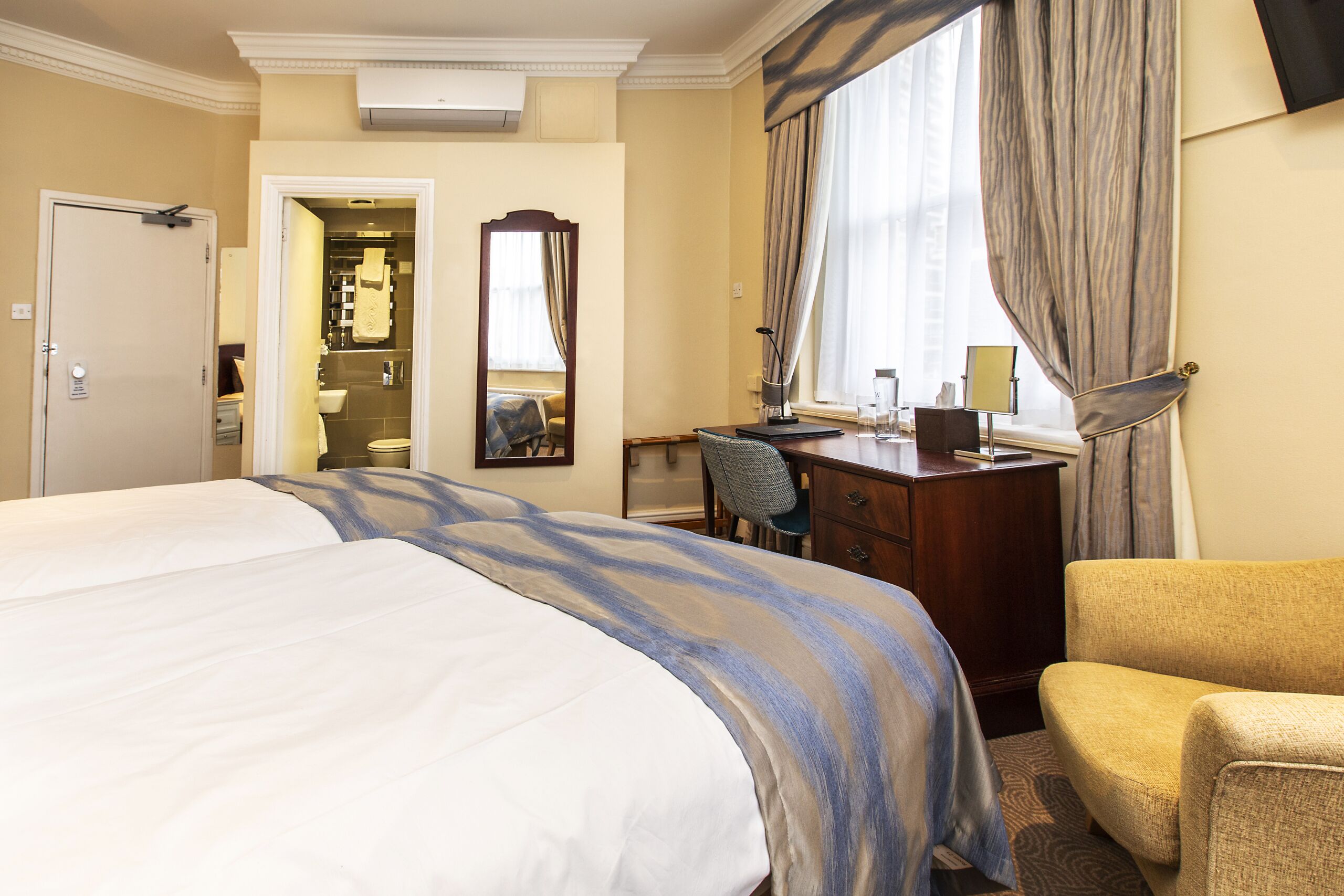 A hotel room with a large bed, a desk, a chair, a mirror, and a window with curtains.