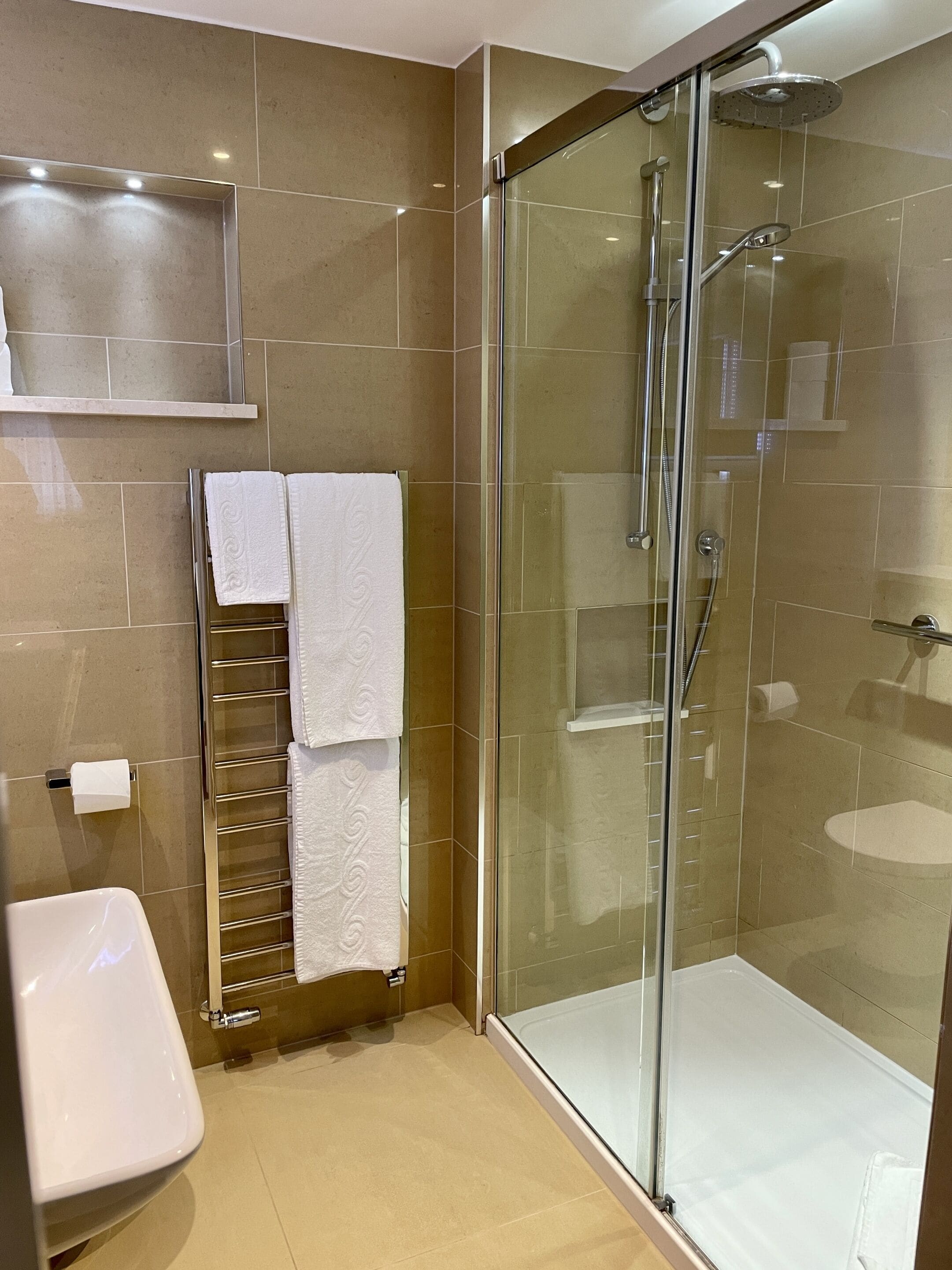 A modern bathroom with a glass-enclosed shower, a white sink, and a towel rack with multiple towels.