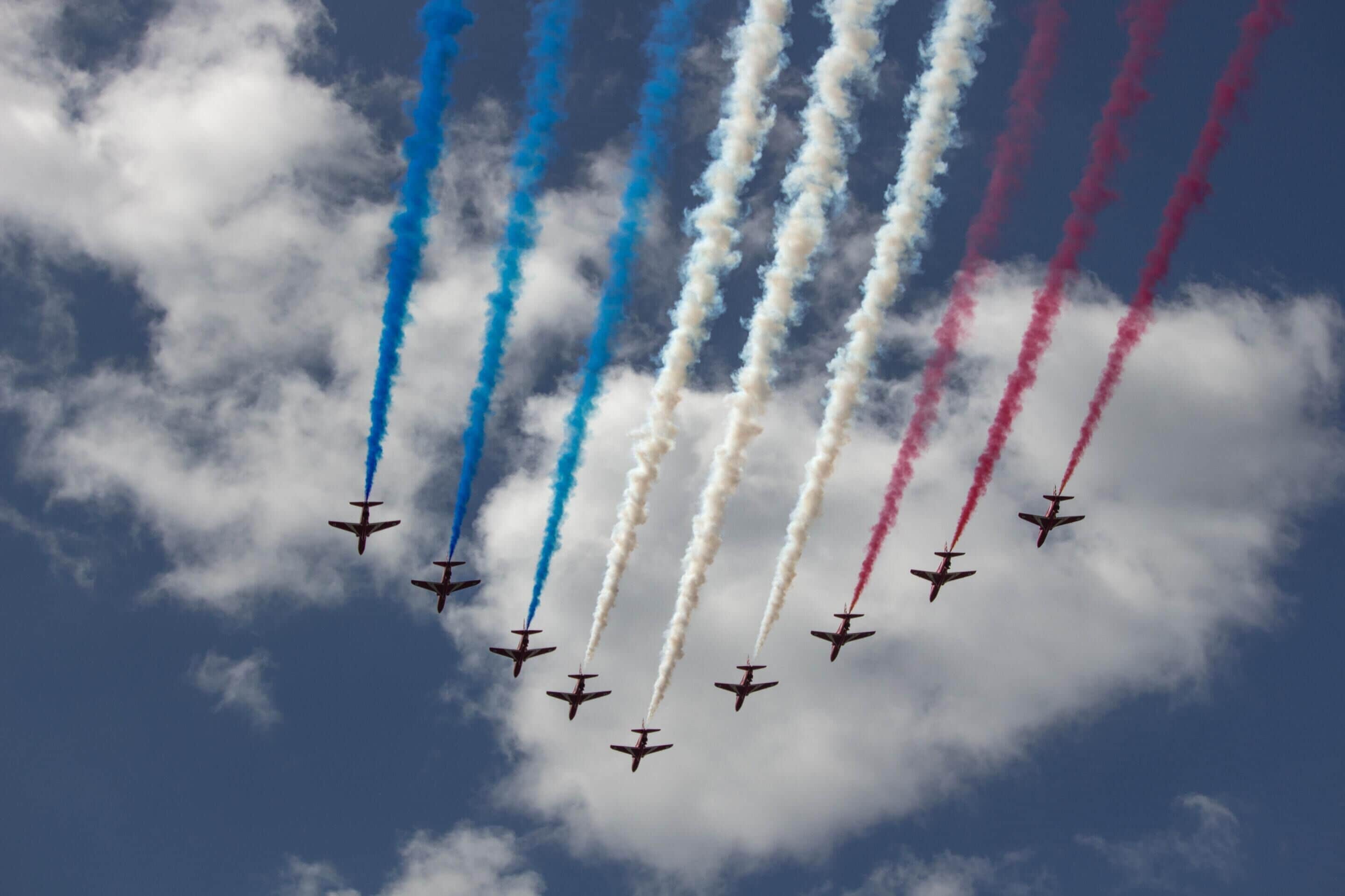 Una formación de aviones volando en un cielo despejado con estelas de humo de colores vivos.