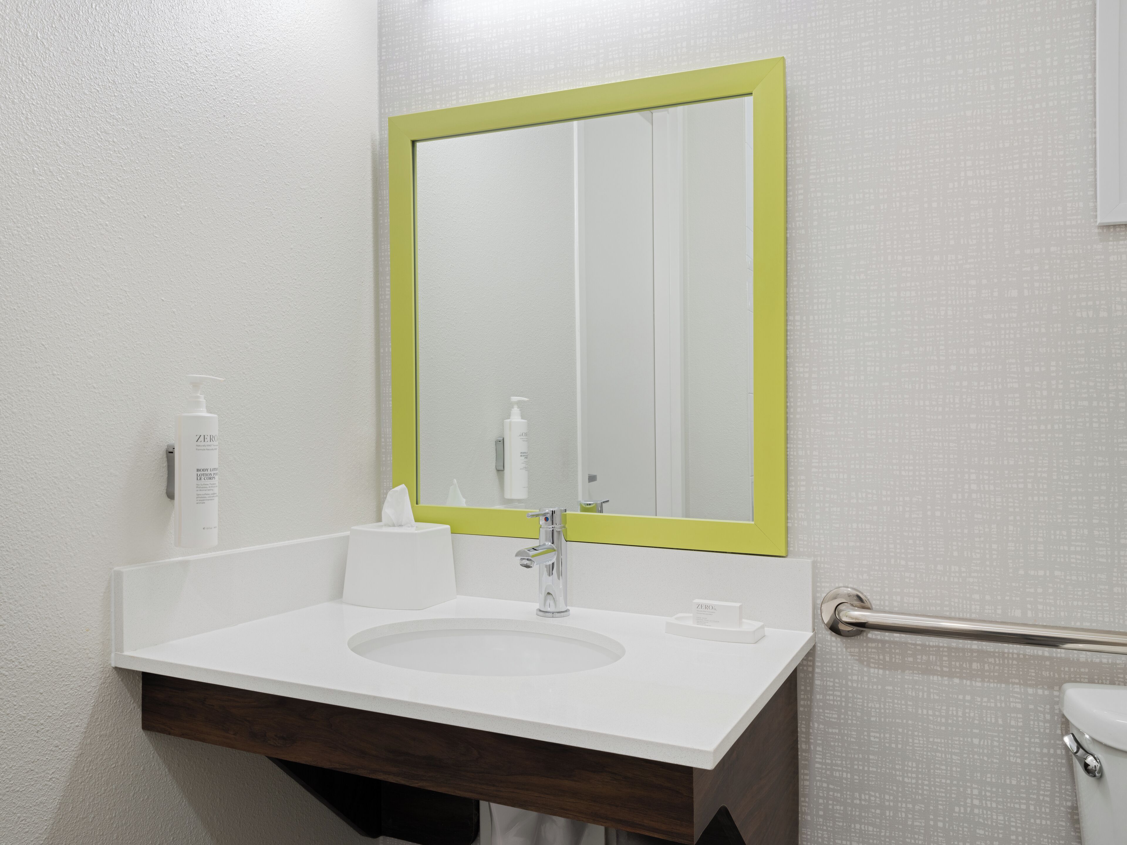 A bathroom with a white sink, a mirror with a green frame, and a white towel dispenser.