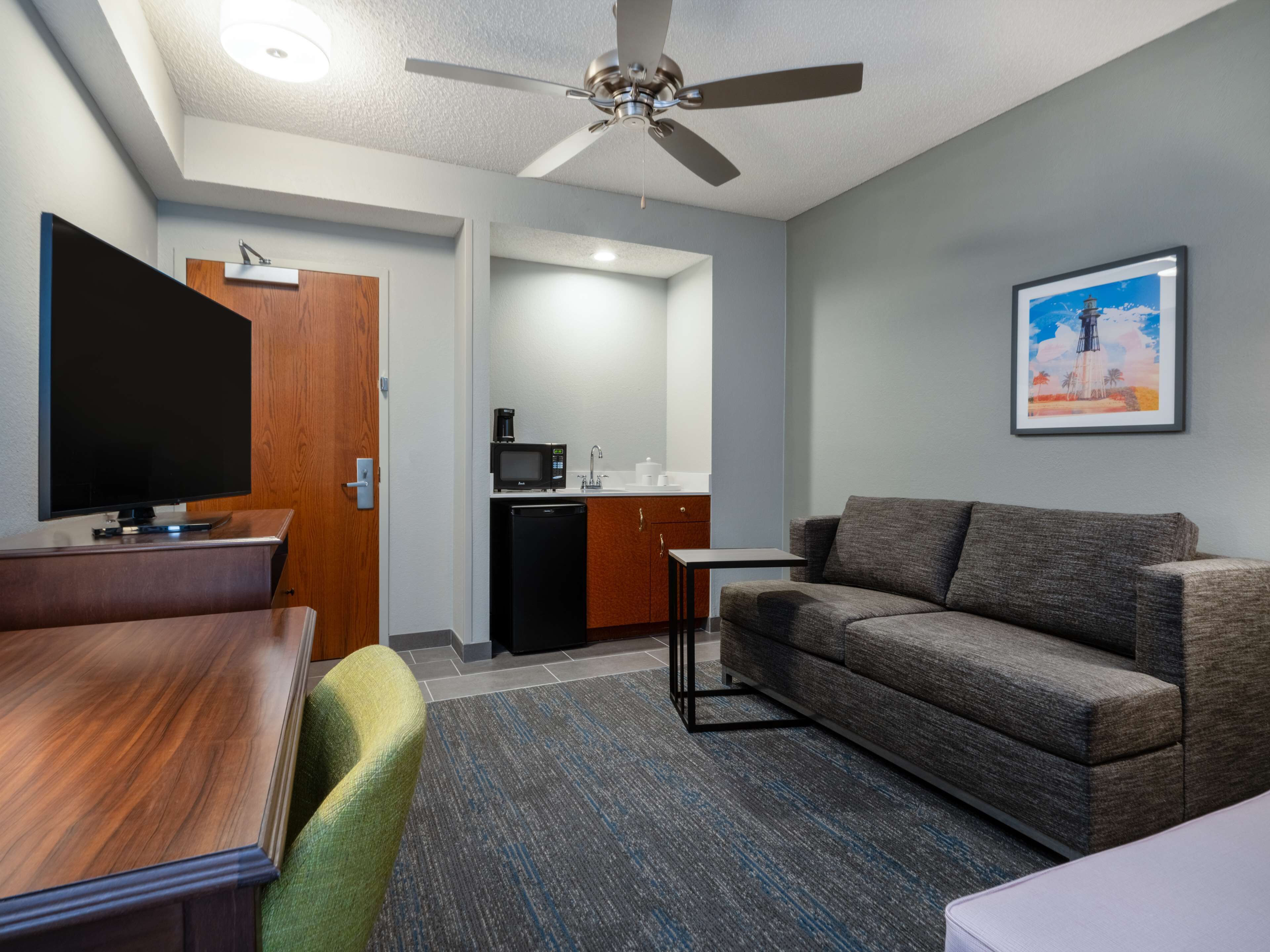 A compact living space with a flat-screen TV, a kitchenette, a sofa, and a ceiling fan.