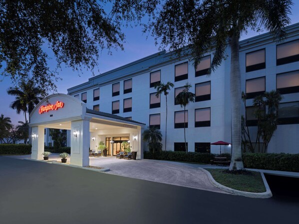 A hotel entrance with a clear sign, paved driveway, and palm trees.