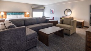 A modern hotel room with a sectional sofa, a single armchair, a small table, and a round mirror. - Hampton Inn Boca Raton-Deerfield Beach (Deerfield Beach)
