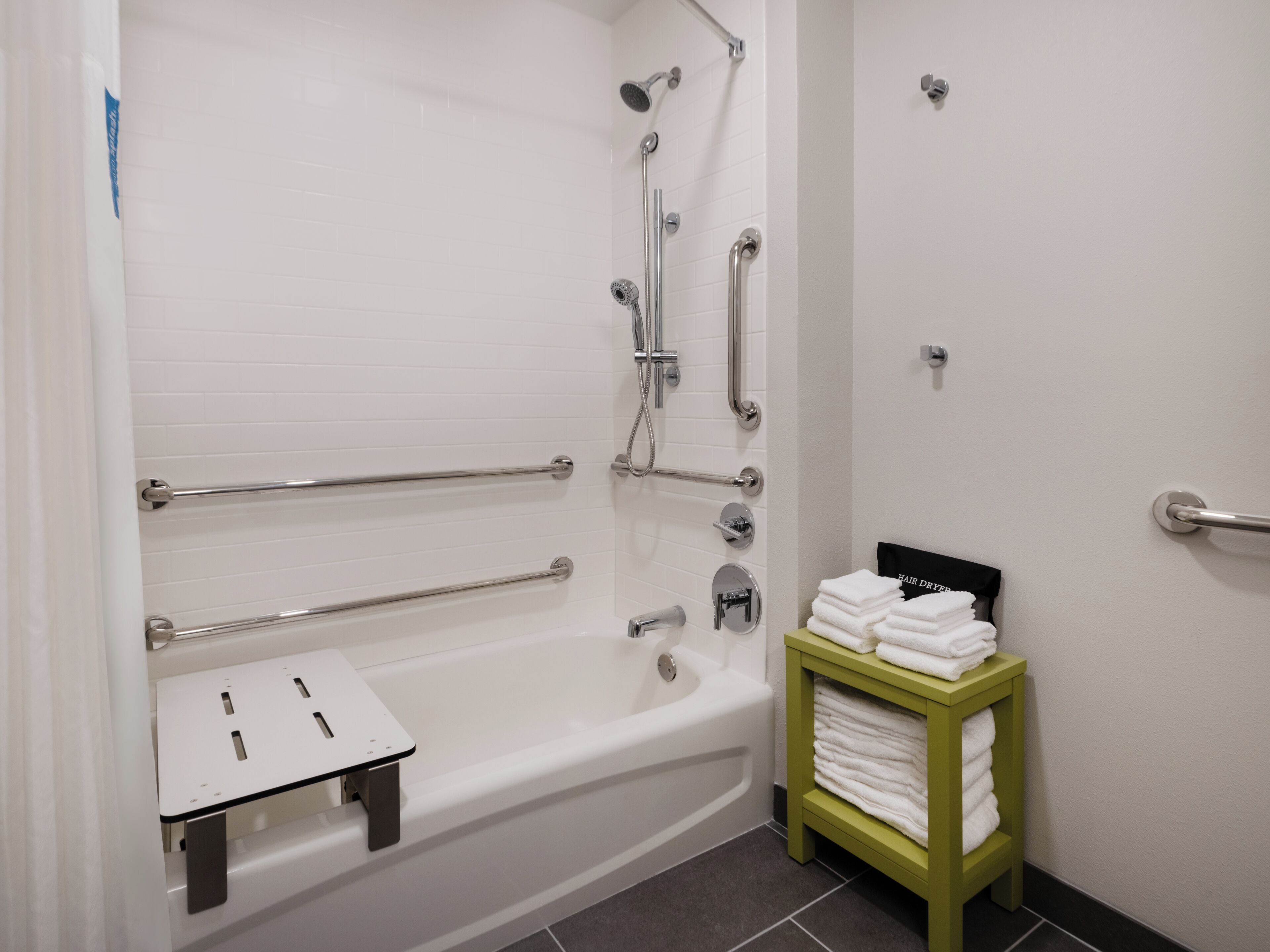 Un baño moderno con cabina de ducha, barras de apoyo, un perchero y una mesita con toallas.