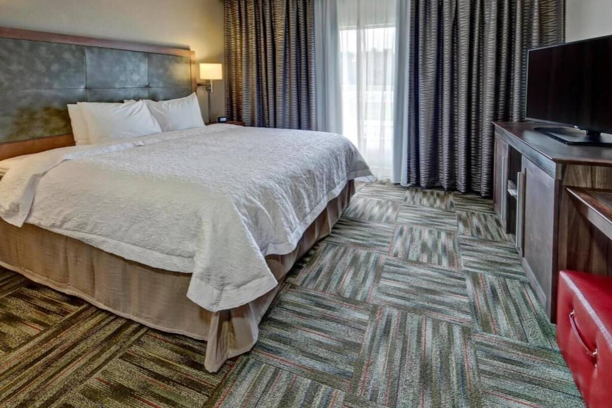 A hotel room with a large bed, a television, a desk, and a red chair.