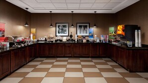 A spacious kitchen area with a checkered floor, wooden cabinets, and various food and beverage dispensers. - Hampton Inn Newberry-Opera House (Newberry)
