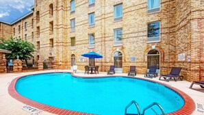 A swimming pool with lounge chairs and umbrellas, surrounded by a brick building with multiple windows and doors. - Hampton Inn Newberry-Opera House (Newberry)