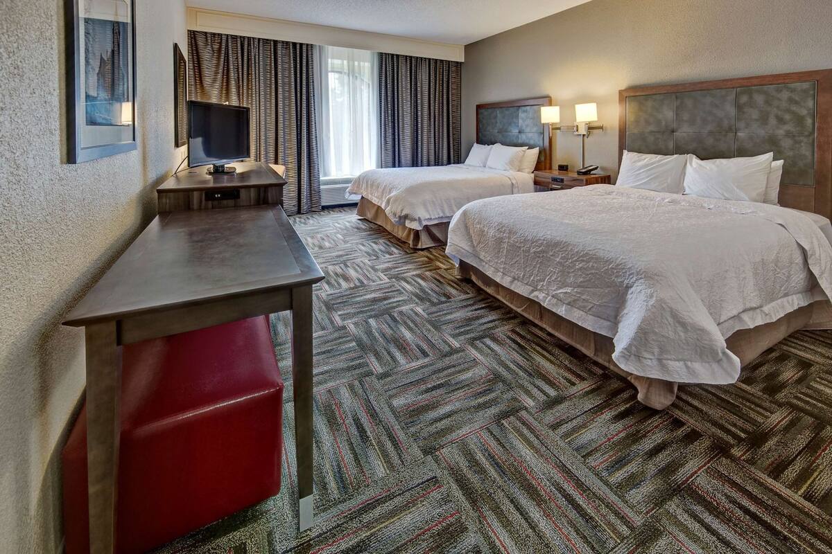 A hotel room with two beds, a desk, a TV, and a red chair.