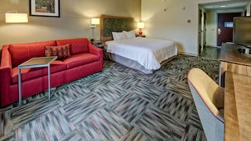 Een hotelkamer met een rode bank, een bed met witte beddengoed, een bureau met een laptop en een televisie.