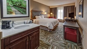A hotel room with a large bed, a desk, a red chair, a TV, and a bathroom with a sink and mirror. - Hampton Inn Newberry-Opera House (Newberry)