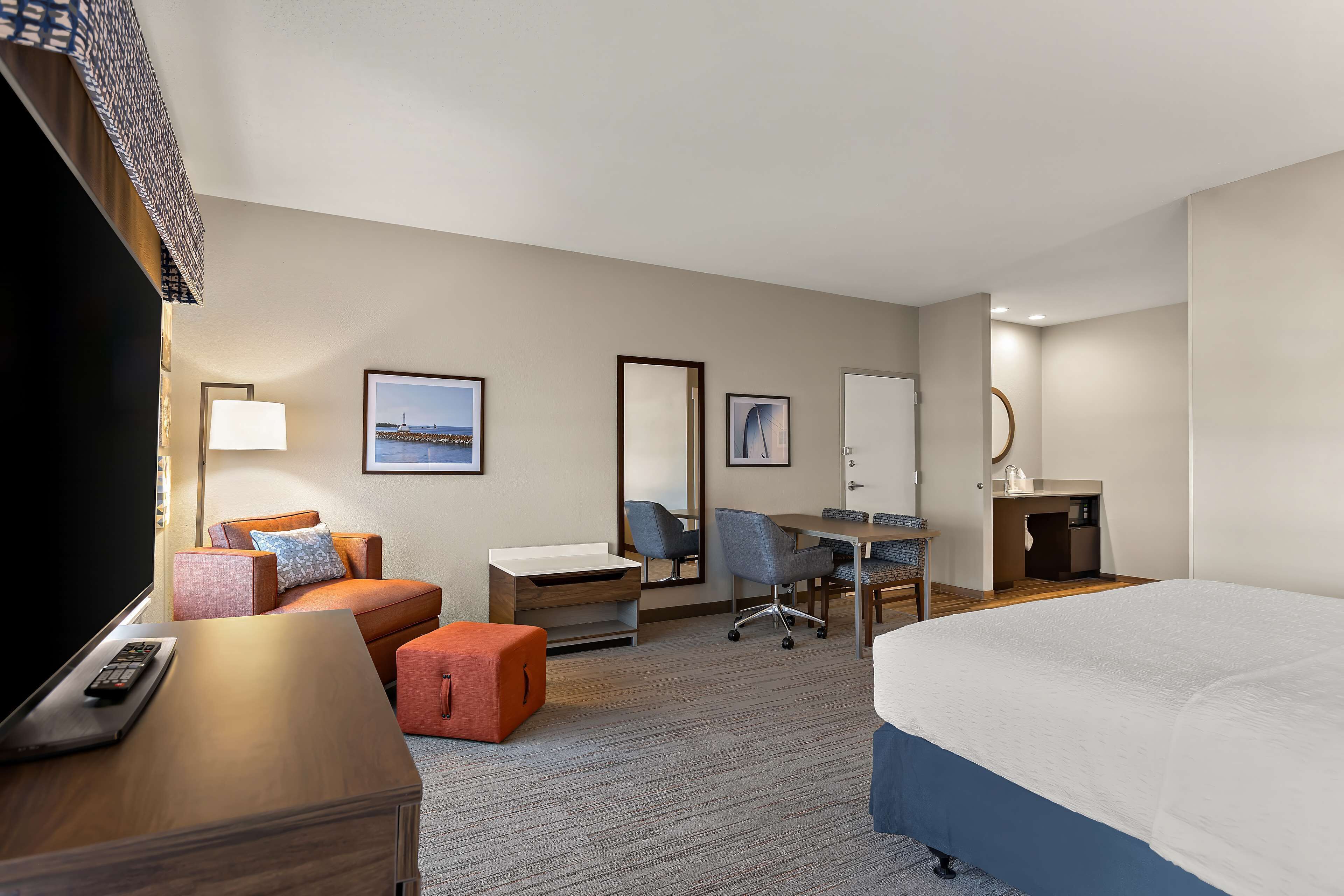 A hotel room with a large bed, a desk with a chair, a television, a sofa, and a small table with a lamp.