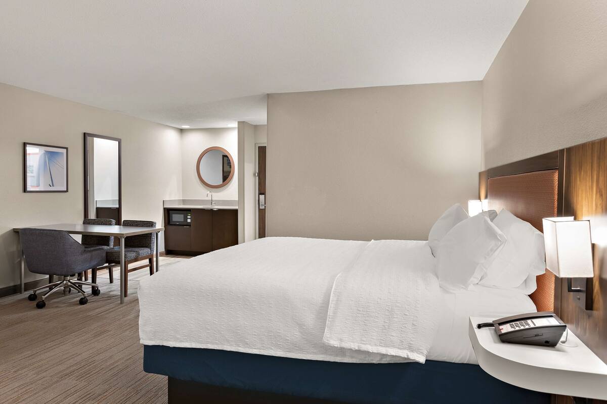 Quarto de hotel com cama, escrivaninha, cadeira e espelho redondo.