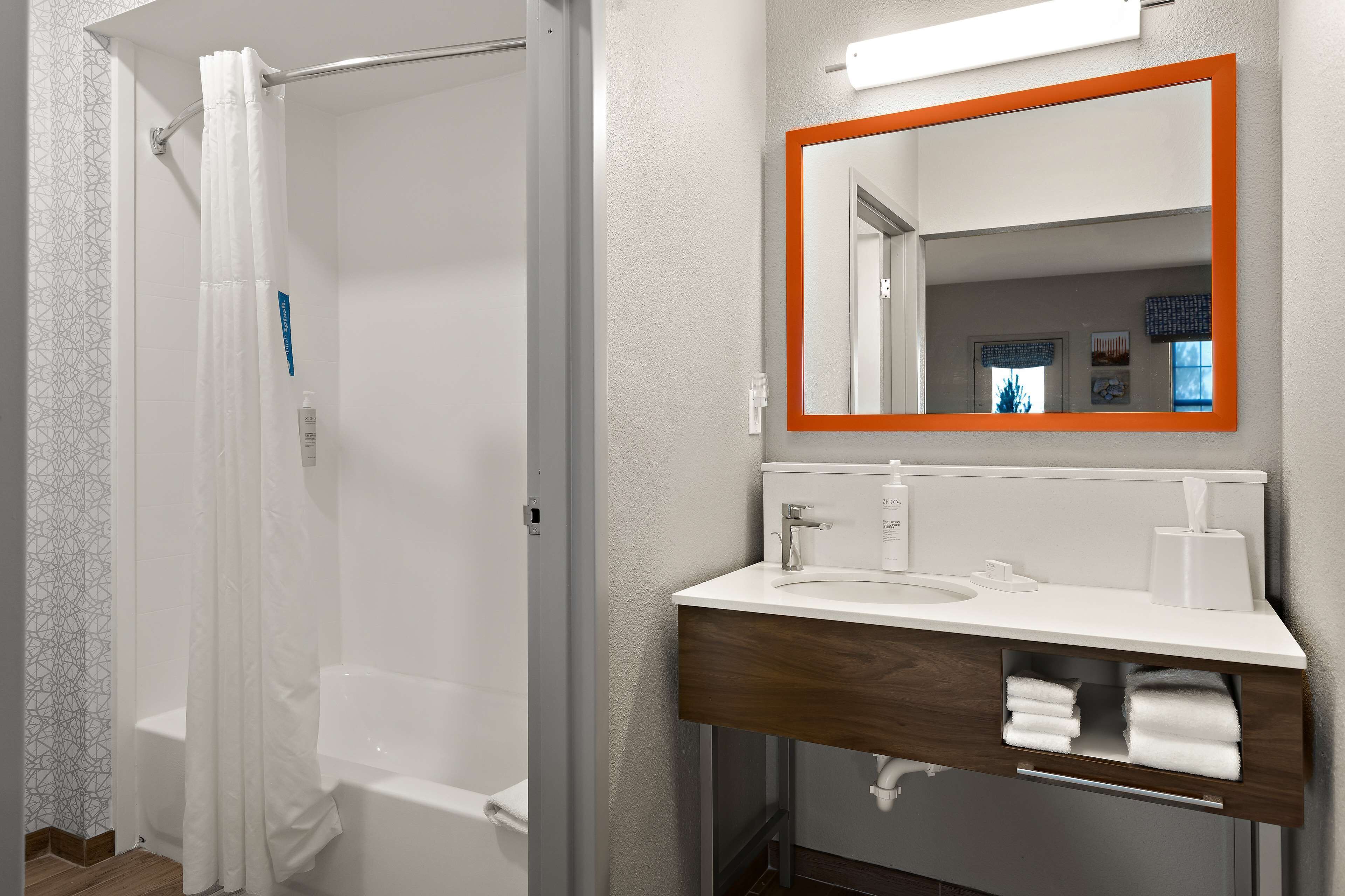 Un baño con ducha, lavamanos, espejo y toallero.