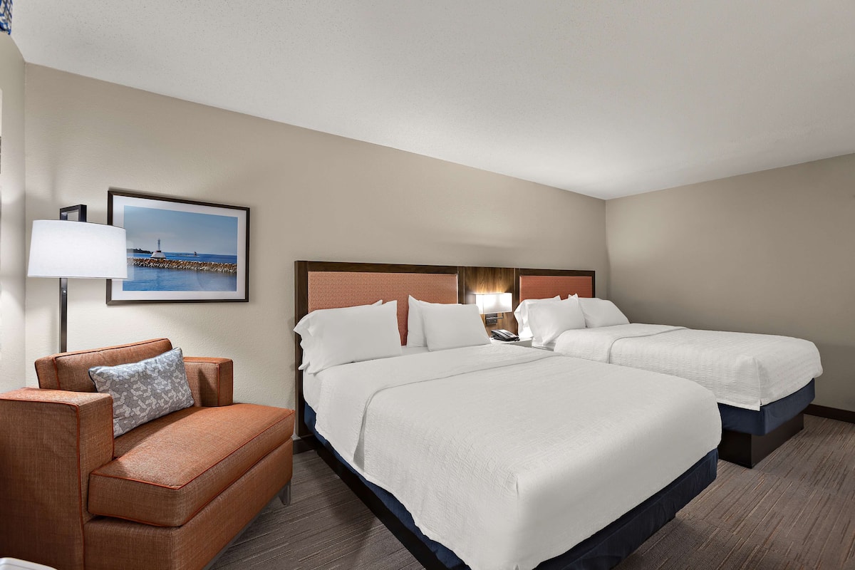 Quarto de hotel com duas camas, um sofá e uma mesa de cabeceira com abajur.