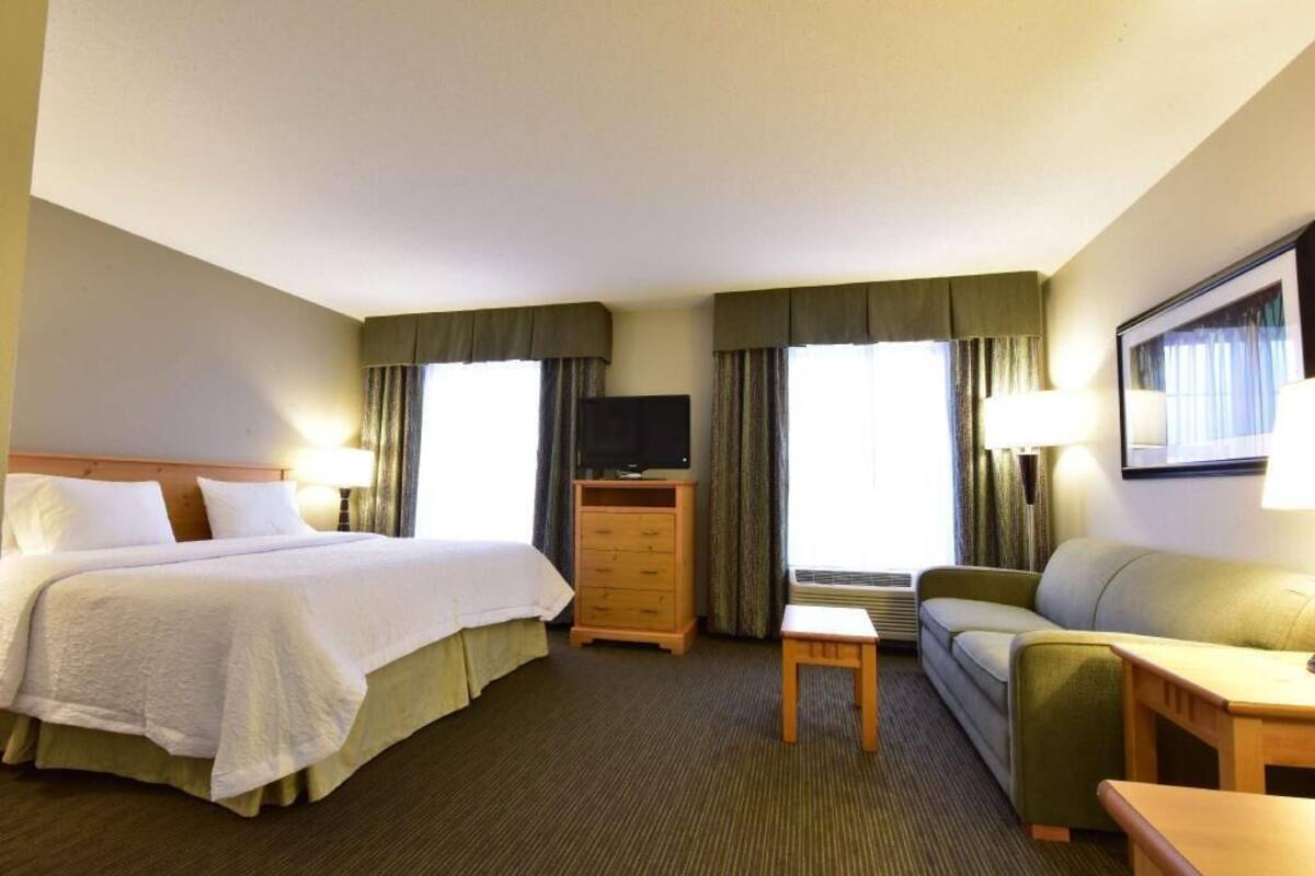 Quarto de hotel com uma cama, televisão, sofá, mesa pequena e cômoda.