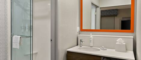 A modern bathroom with a glass shower enclosure, a white sink with a wooden vanity, and a mirror with an orange frame.