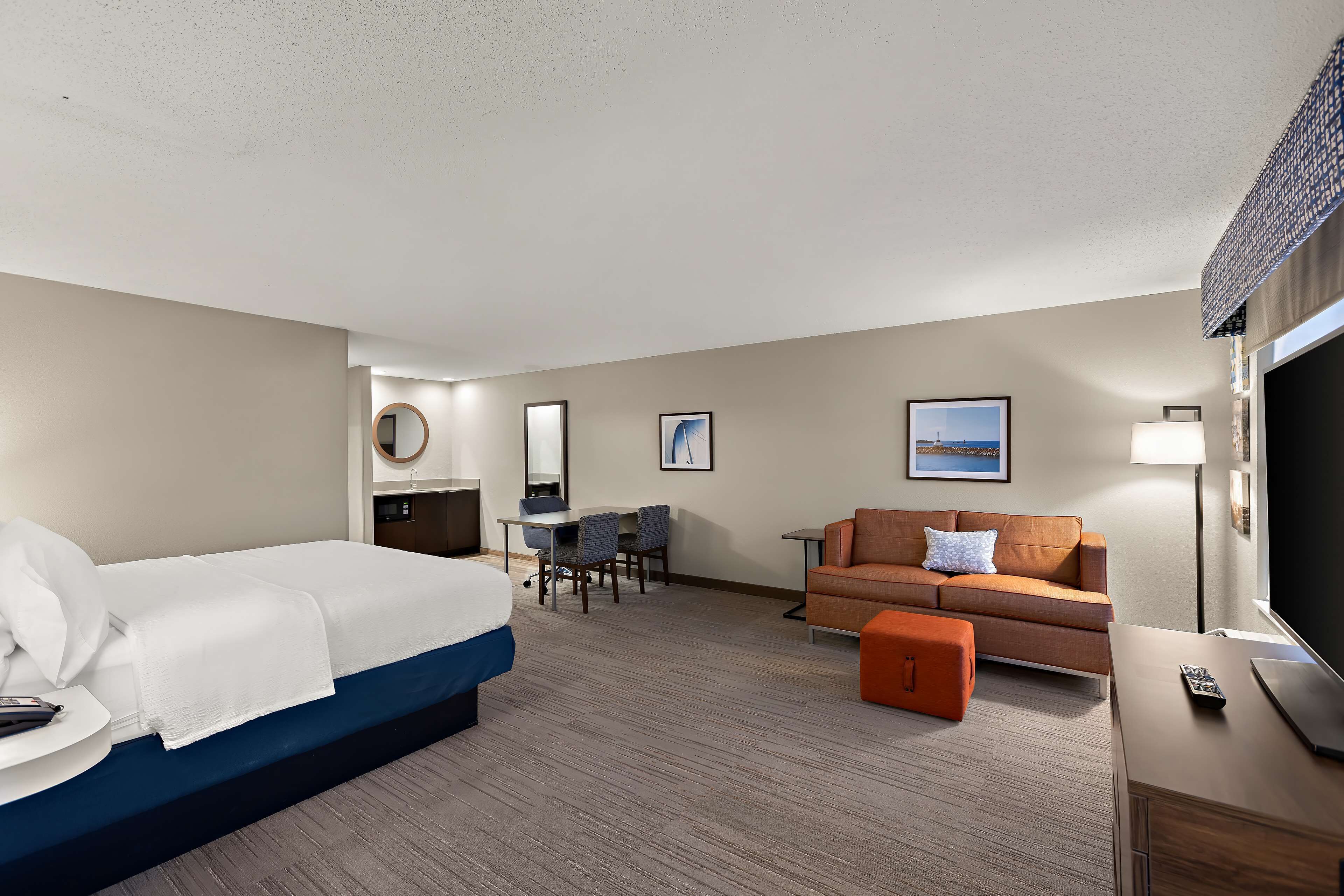A hotel room with a bed, a desk with chairs, a sofa, a TV, and a lamp.