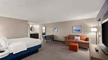 A hotel room with a bed, a desk with chairs, a sofa, a TV, and a lamp.
