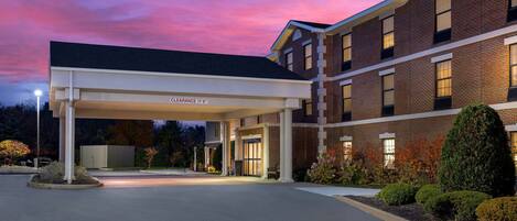 A hotel entrance with a covered driveway, brick facade, and landscaped garden.