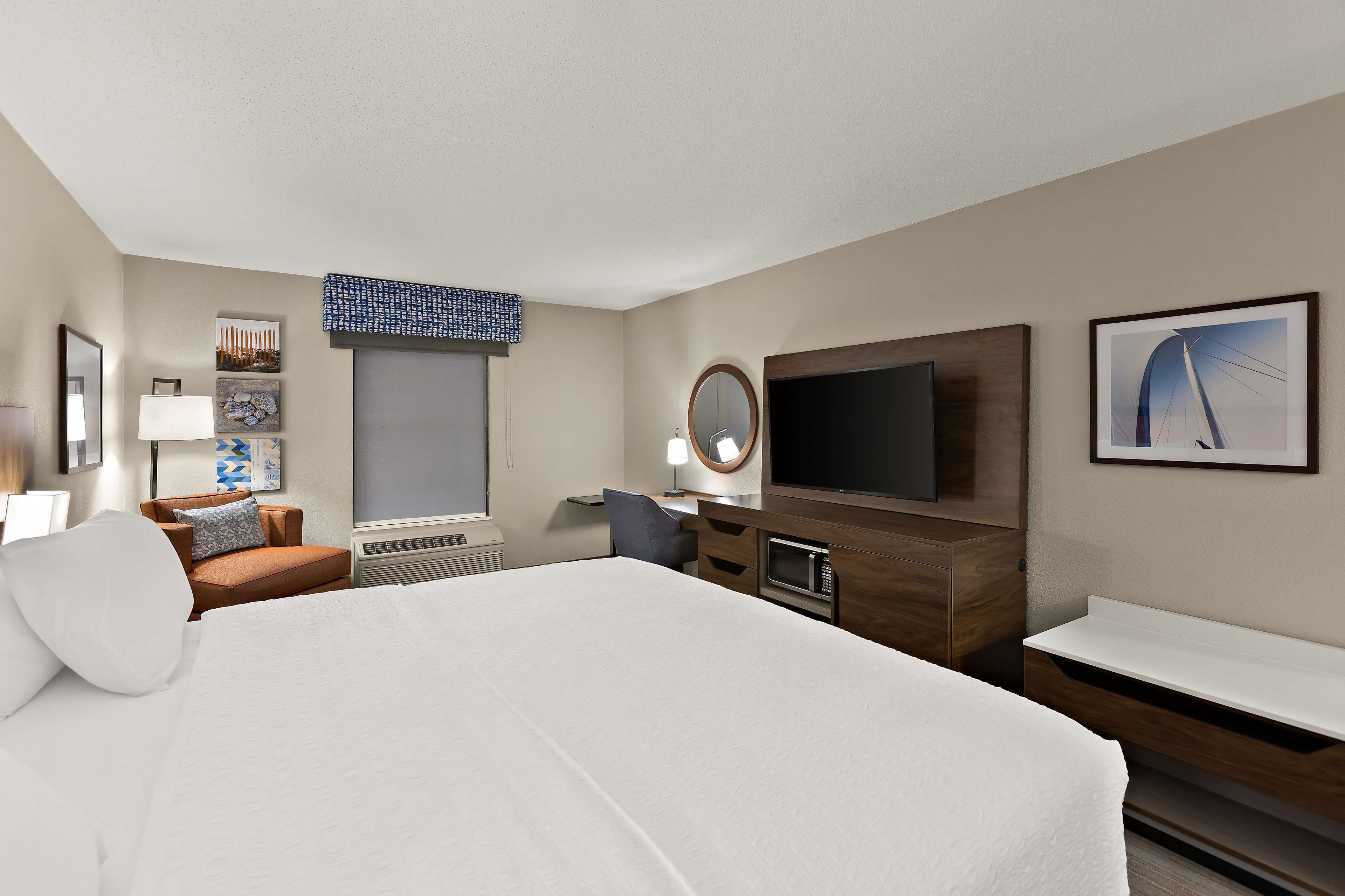 A hotel room with a large bed, a desk with a computer, a TV, and a window with blinds.