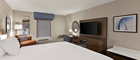 A hotel room with a large bed, a desk with a computer, a TV, and a window with blinds.