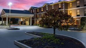 Ein mehrstöckiges Hotel mit überdachter Eingangspartei, angelegtem Garten und einem Baum im Vordergrund.