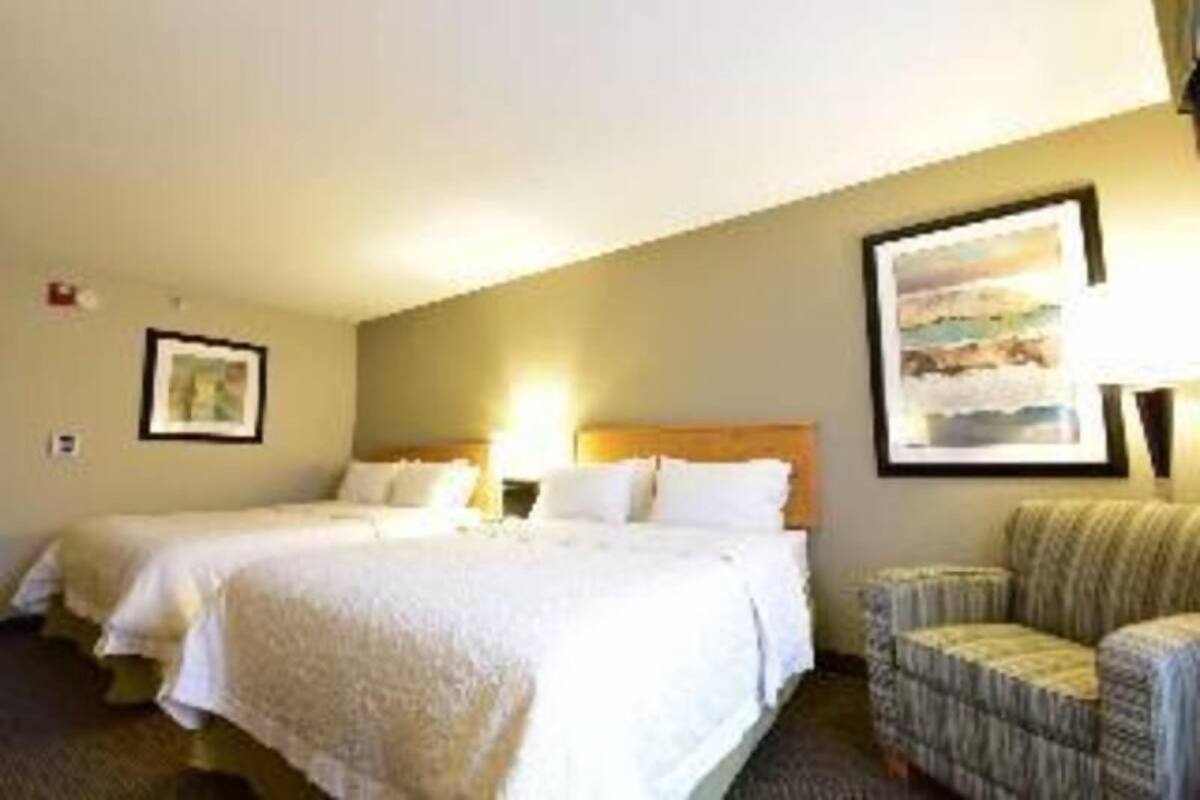 Quarto de hotel com duas camas, uma cadeira e um quadro na parede.