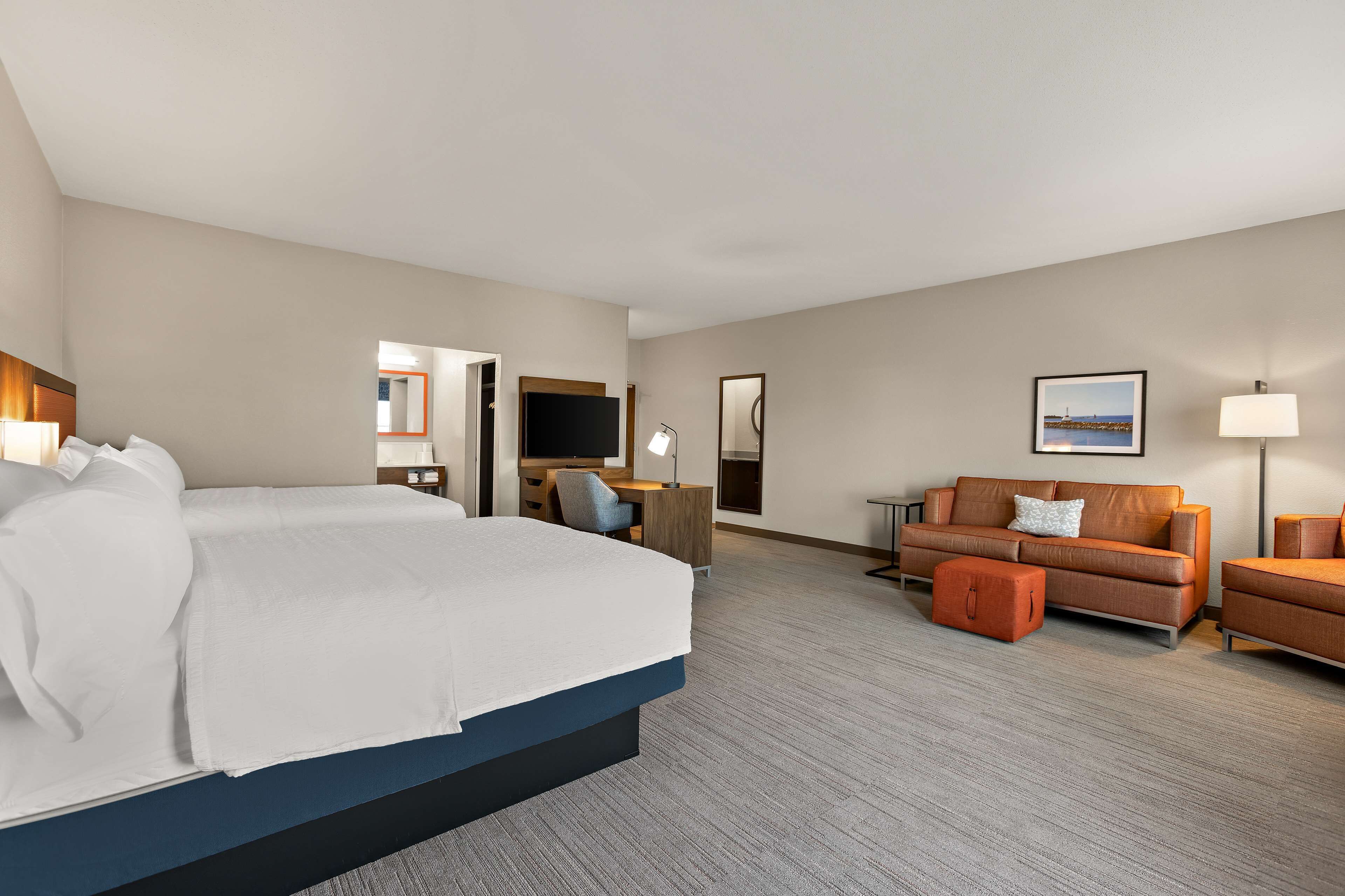 A hotel room with a large bed, a sofa, a desk, and a chair. There is a TV, a lamp, and a framed picture on the wall.
