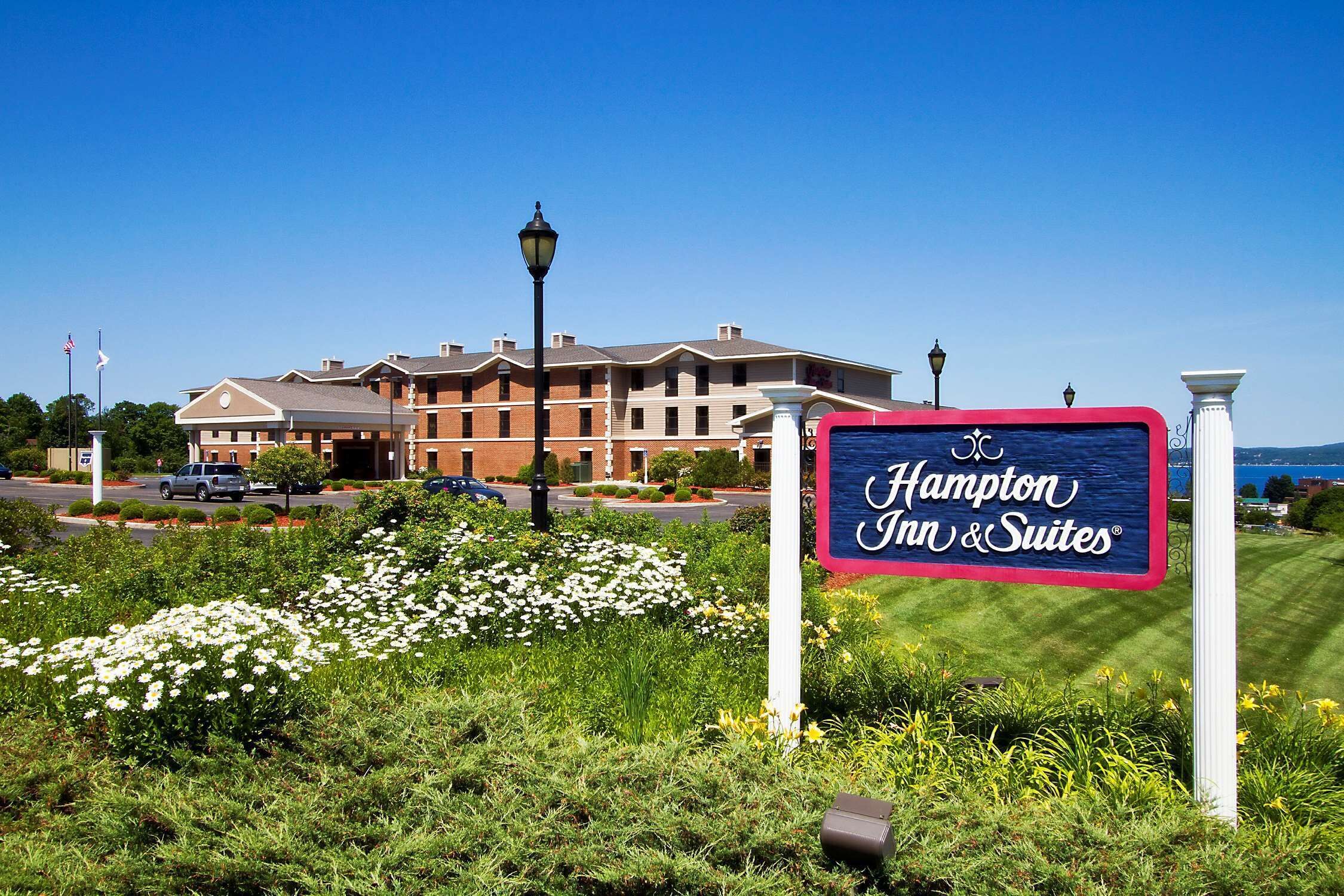 A Hampton Inn & Suites sign with a view of the hotel and surrounding greenery.