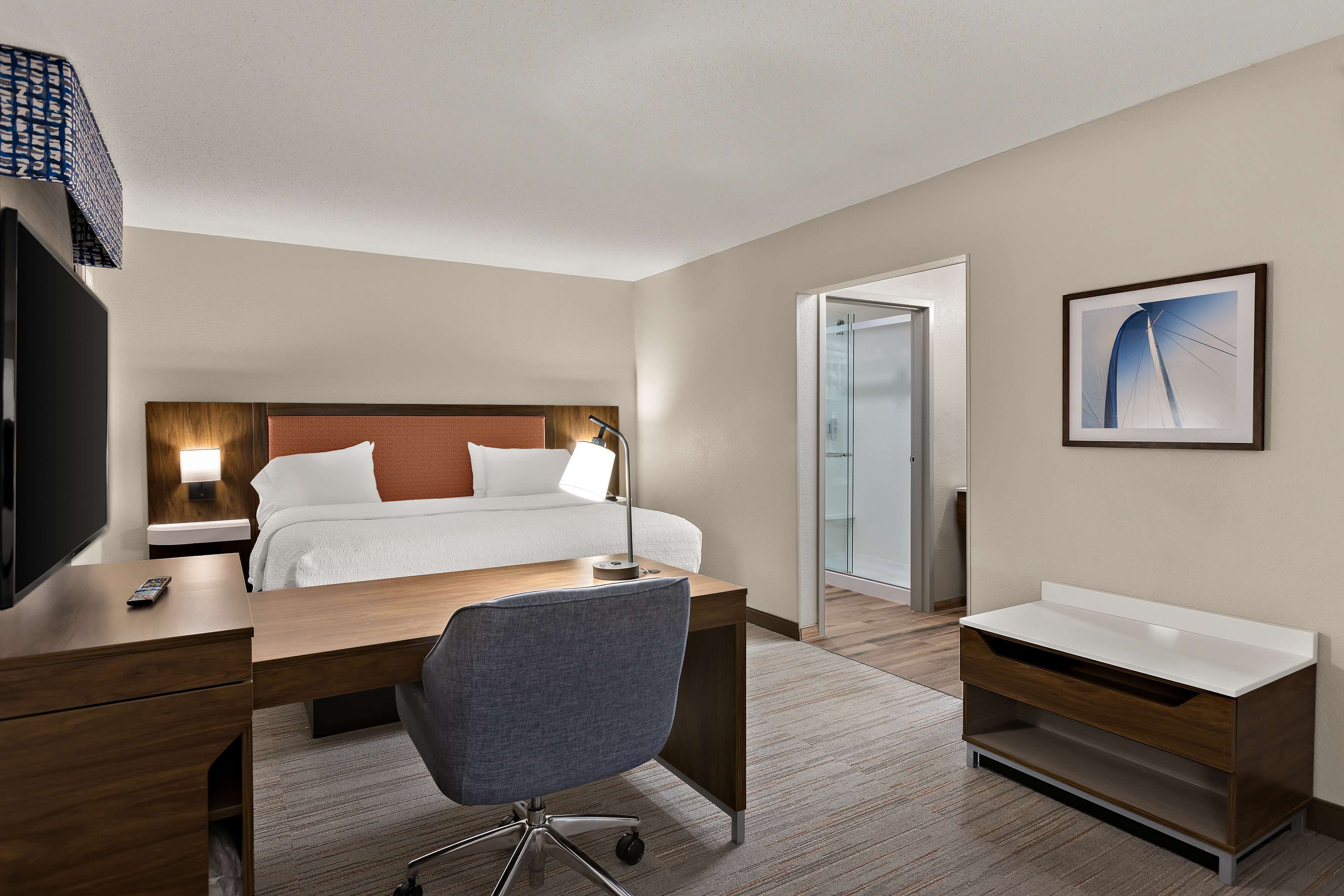 Ein Hotelzimmer mit Bett, Nachttisch, Schreibtisch, Stuhl und einem kleinen Badezimmer.
