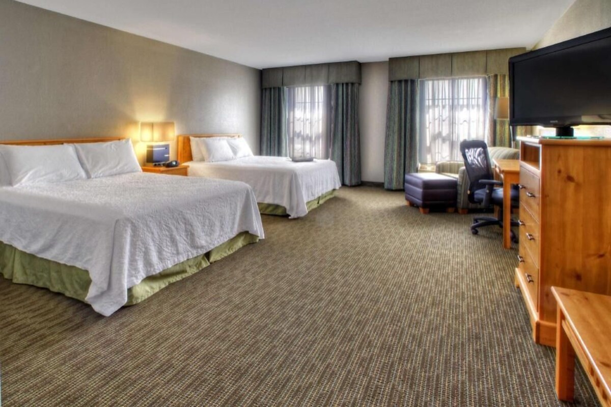 A hotel room with two beds, a desk, a chair, a television, and a dresser.