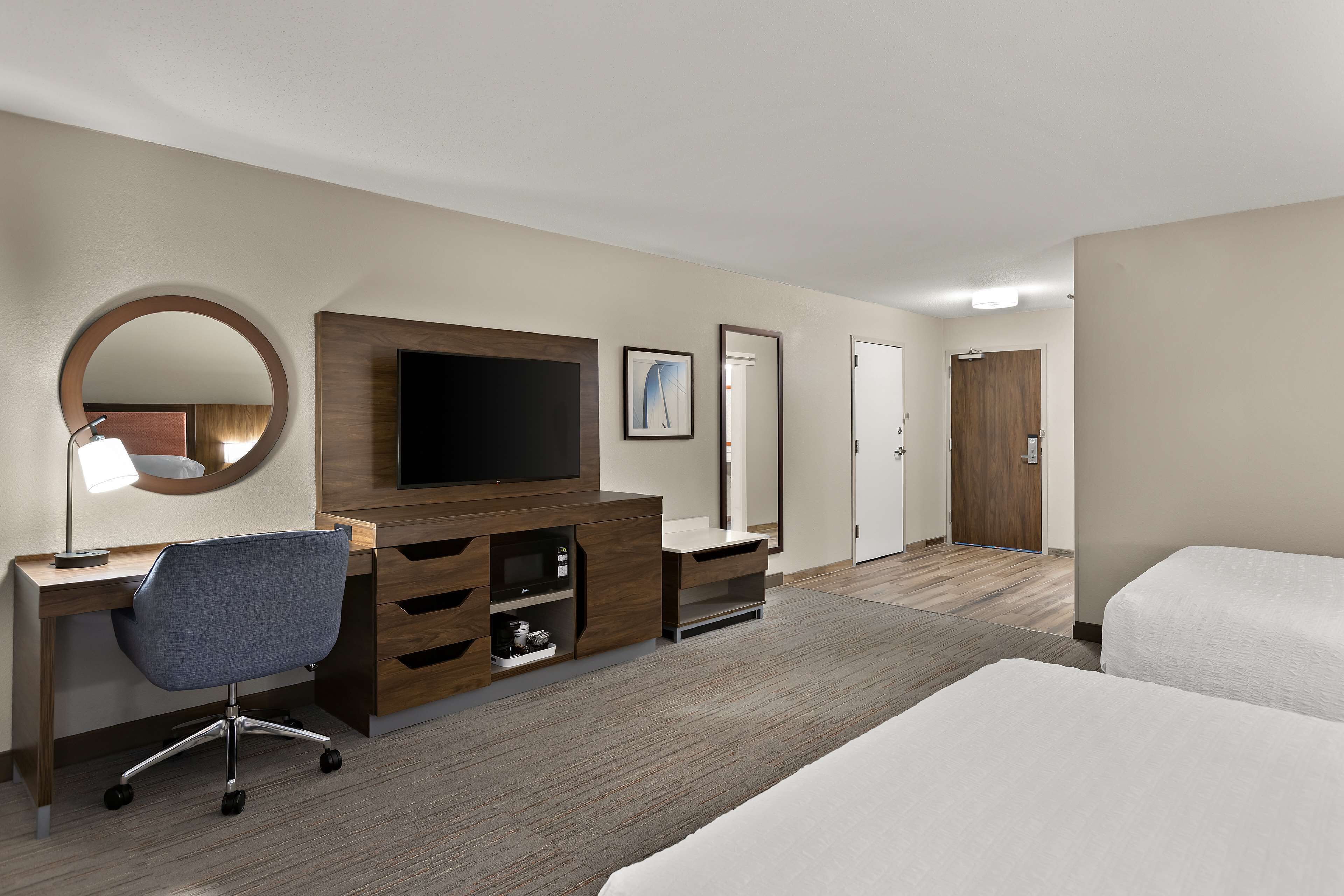 A hotel room with a desk, chair, TV, and a bed.
