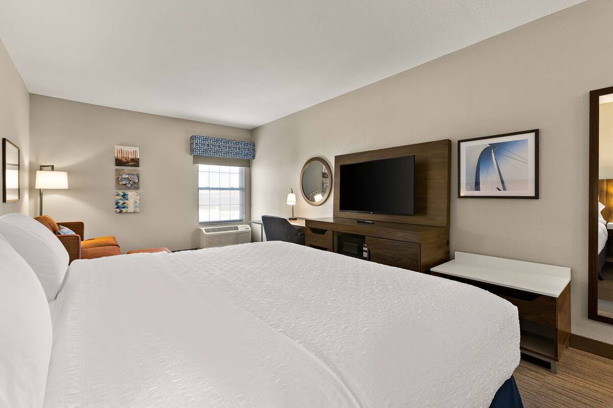 Quarto de hotel com uma cama grande, uma escrivaninha, televisão, espelho e janela com vista.