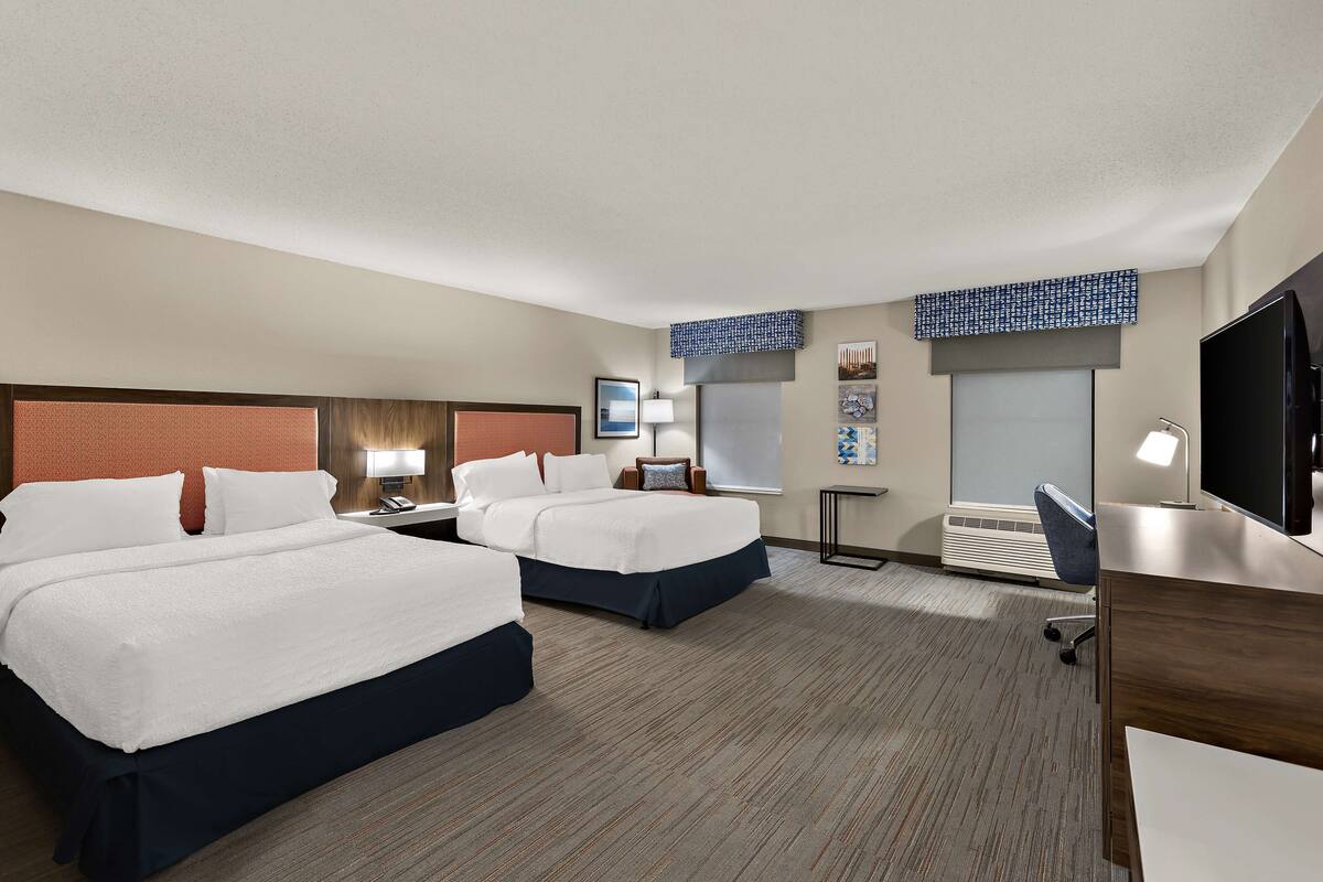 Quarto de hotel com duas camas, uma escrivaninha, televisão e janela.