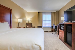 A hotel room with a large bed, a desk with a computer, a television, and a chair.