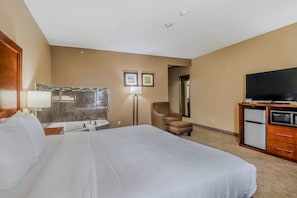 A hotel room with a large bed, a desk with a lamp, a chair, a television, and a refrigerator.