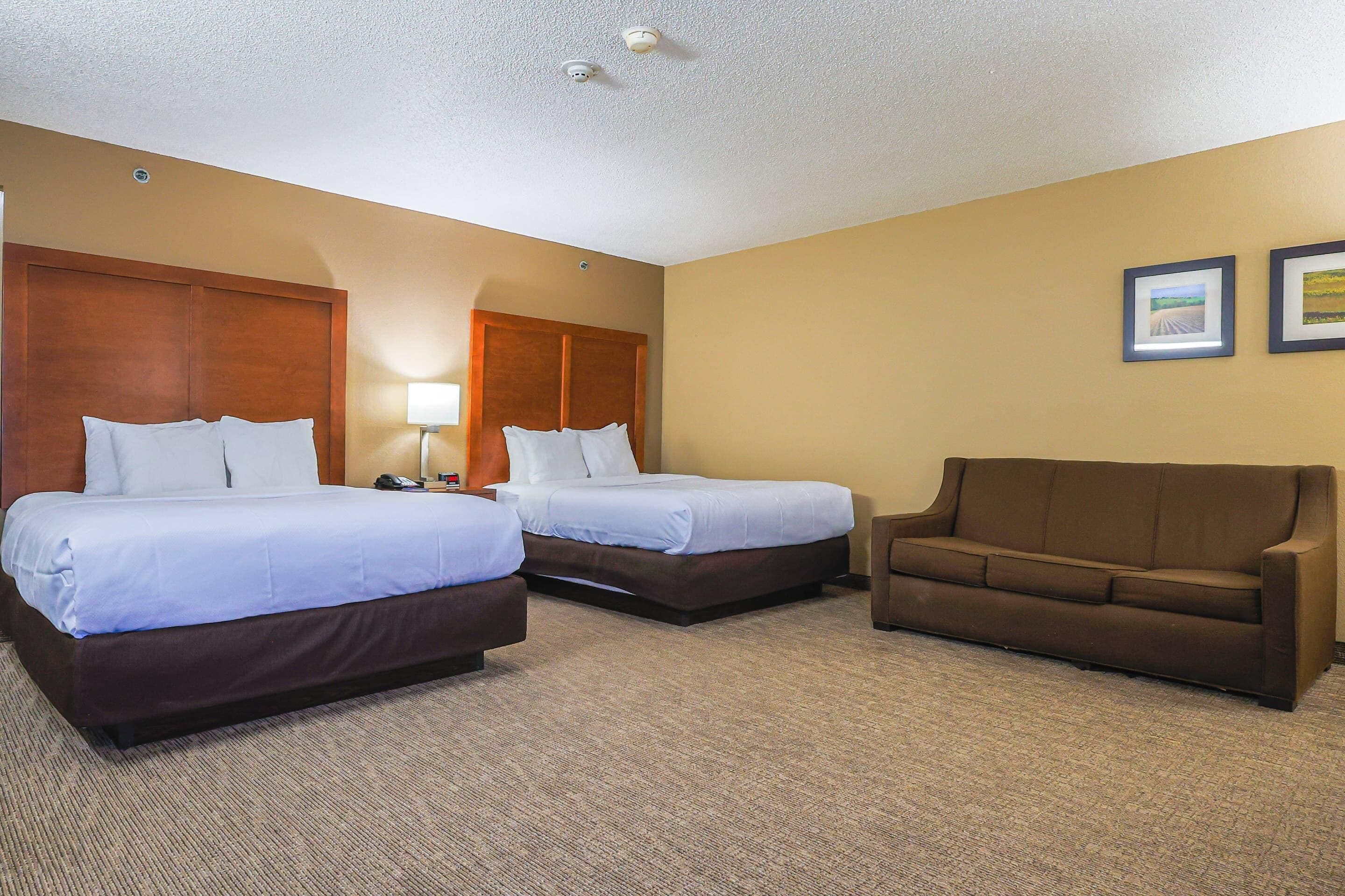 A hotel room with two beds, a brown sofa, and two framed pictures on the wall.