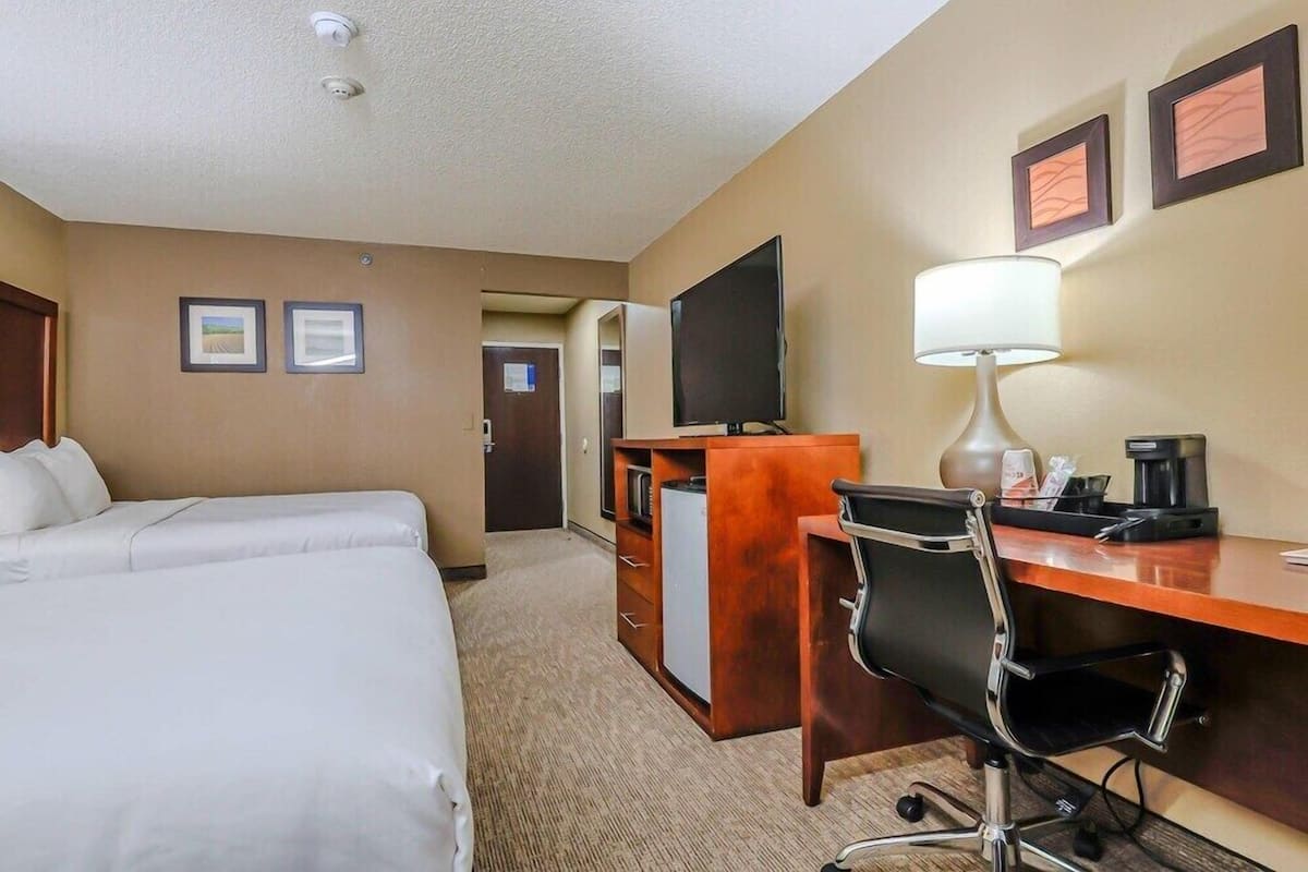 Una habitación de hotel con dos camas, un escritorio con silla, televisor, lámpara y cafetera.