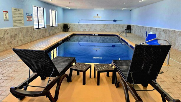 Piscina interior com chão de azulejos, escada para piscina e alguns cadeiras e mesas.