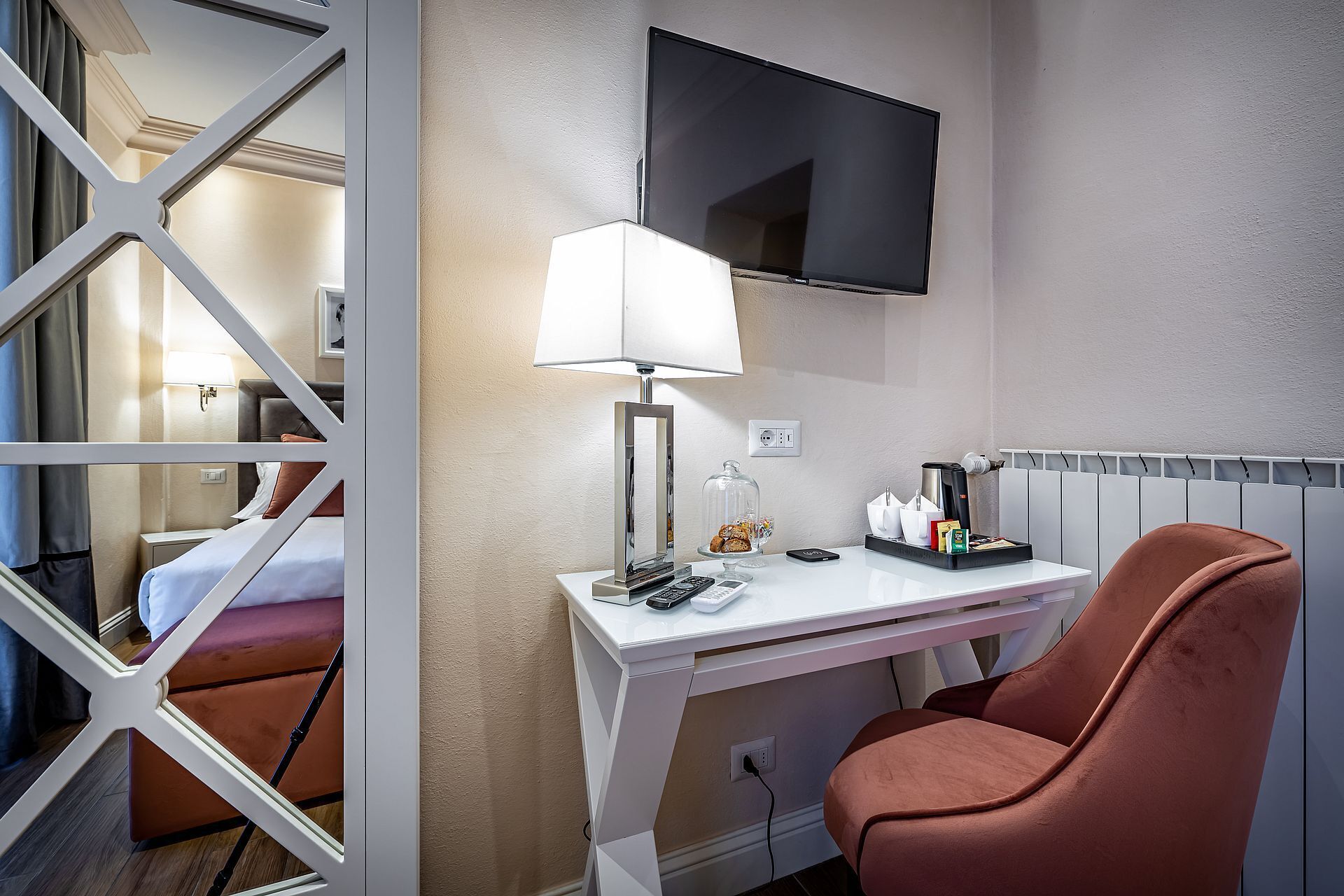 Une chambre d’hôtel équipée d’un bureau, d’une chaise, d’un téléviseur fixé au mur, d’une lampe et d’un lit doté de rideaux.